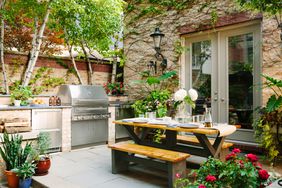 Backyard patio with outdoor dining table and large stainless steel grill.
